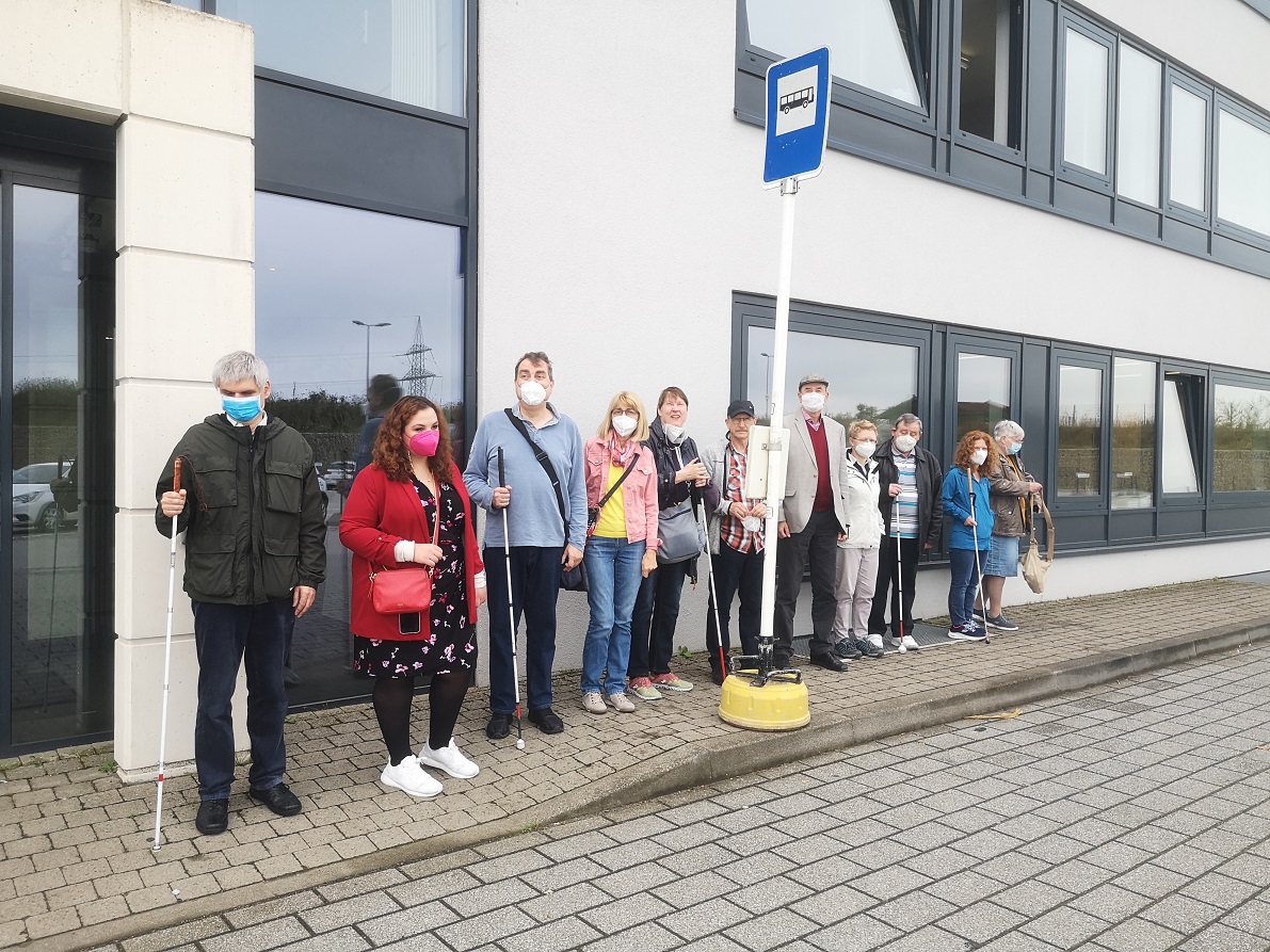 A mixed group of participants, some with white canes, waiting at a bus stop. (Photo Romain Ferretti)